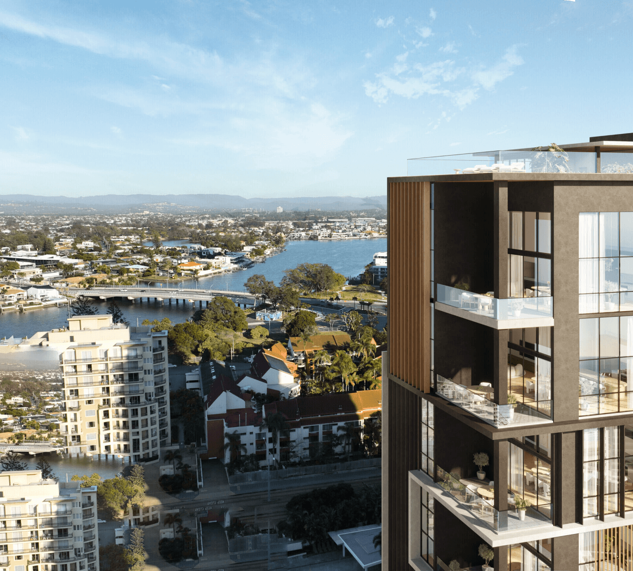 Highly elevated daytime photo on a sunny day. Taller buildings can be seen, especially in the foreground of the photo. The background focus is of a river and more residential buildings. The building at the focus in the foreground takes up a majority of the right half of the image. It depicts a modern building with brown and wooden features, offset against floor to ceiling glass windows. There are balconies on each floor of the building and a terrace on the rooftop. The building appears to be a skyscraper given its height compared to other buildings in the image.
